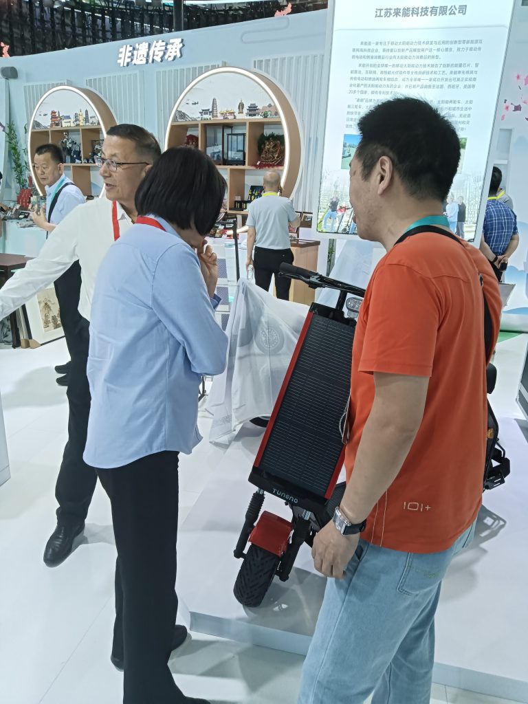 Expo visitors gathering around Tuneng solar kick scooter as staff member explains photovoltaic charging technology features at Laineng Technology booth during Xi'an Silk Road International Exhibition Center trade fair