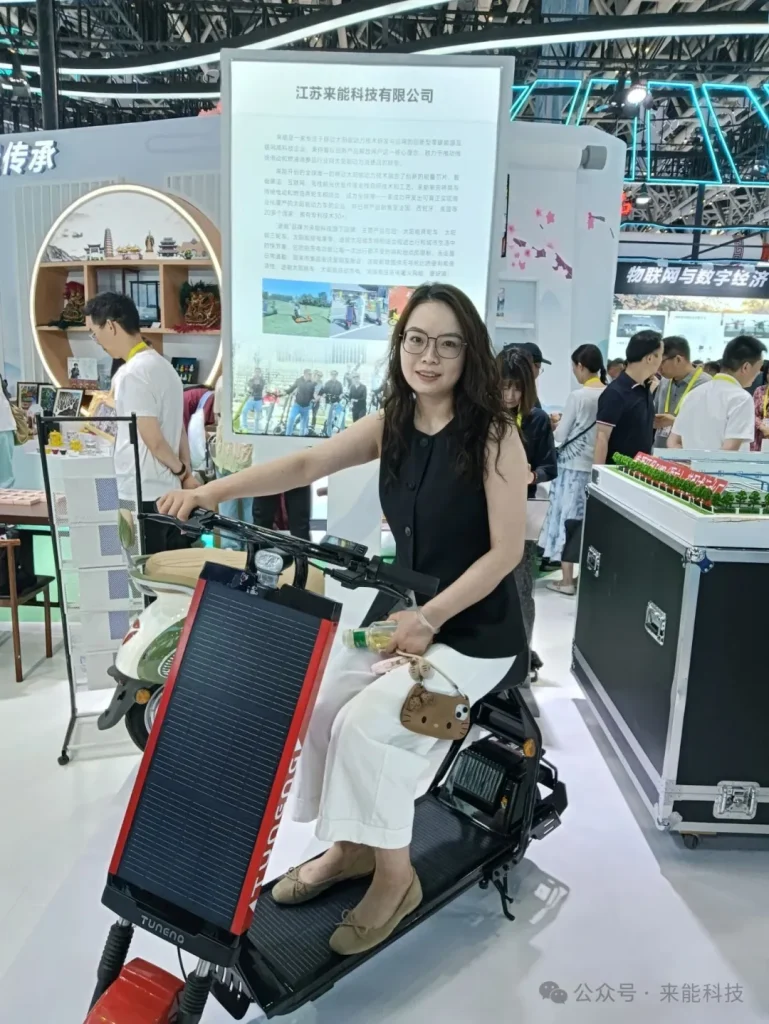 Woman test riding red and black Tuneng T87S Pro solar electric scooter at Laineng Technology booth during 19th China Xi'an Silk Road Expo with Jiangsu Laineng Technology Company introduction board displayed behind