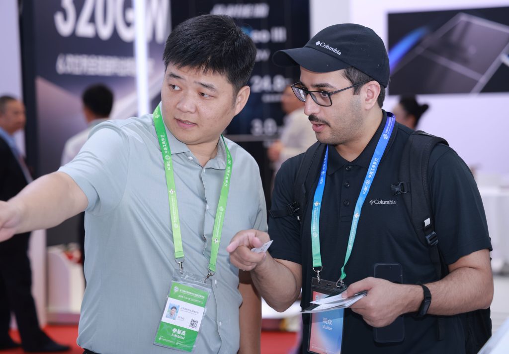 Laineng staff member explaining solar electric scooter specifications to Colombian visitor wearing Columbia cap at CISCE expo booth with product spec board showing battery capacity and range data in background