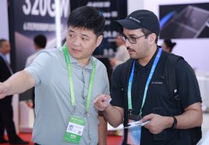 Laineng staff member explaining solar electric scooter specifications to Colombian visitor wearing Columbia cap at CISCE expo booth with product spec board showing battery capacity and range data in background