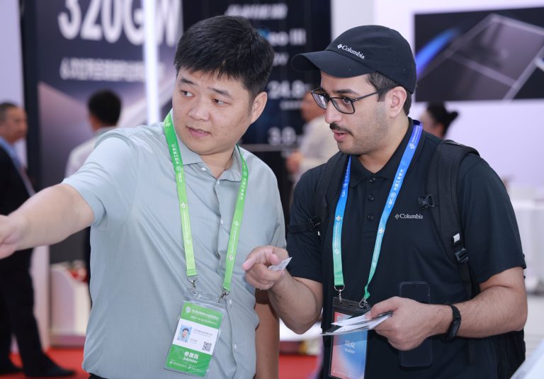 Laineng staff member explaining solar electric scooter specifications to Colombian visitor wearing Columbia cap at CISCE expo booth with product spec board showing battery capacity and range data in background