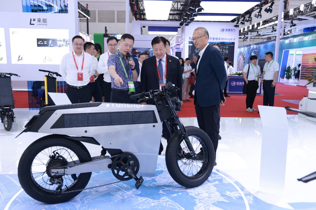 Jiangsu Vice Governor Fang Wei and trade officials visiting Laineng Technology booth at China International Supply Chain Promotion Expo examining Tuneng solar electric motorcycle with integrated photovoltaic panel
