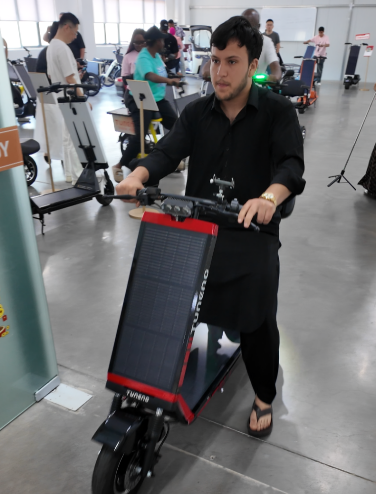 Middle Eastern influencer riding red and black Laineng TUNENG branded solar electric scooter during indoor test ride session at brand center with other visitors testing solar vehicles in background